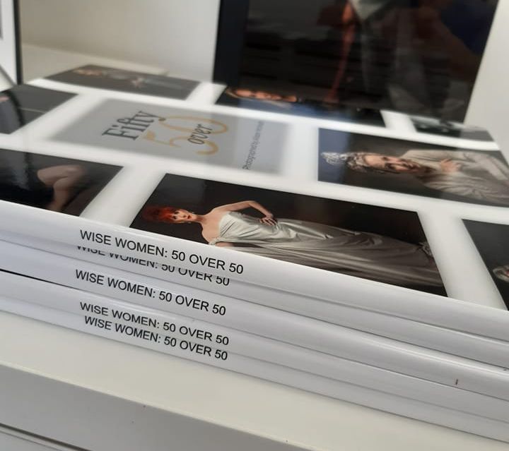 Stack of photography books titled 'Wise Women 50 Over 50' on desk surface.