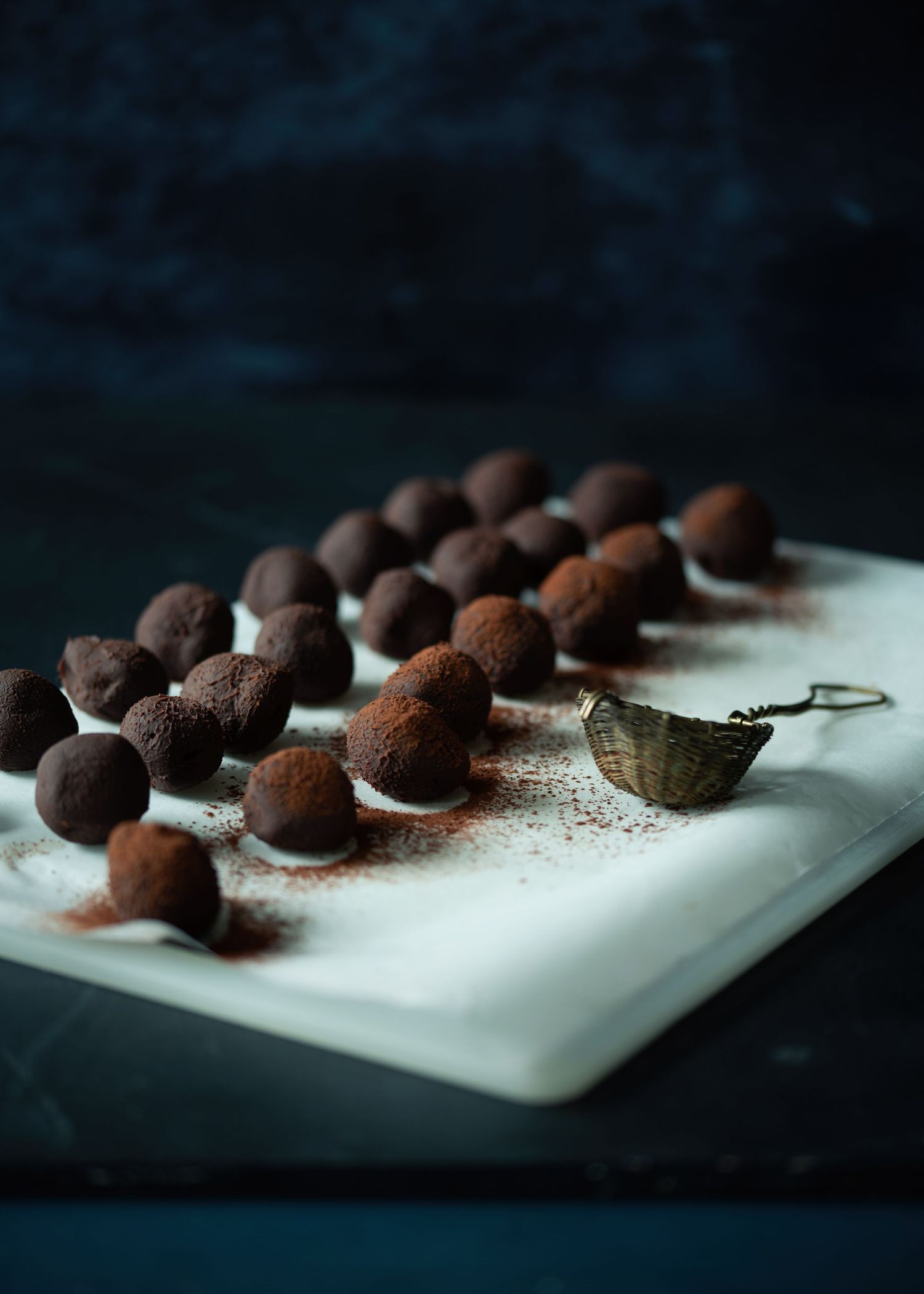 Cocoa-dusted chocolate truffles arranged on a white marble board with a vintage tea strainer.
