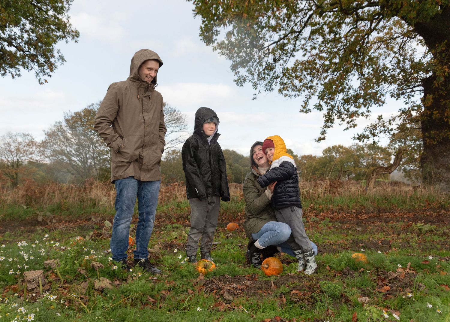 People picking pumpkins in a rustic autumn field on an overcast day.