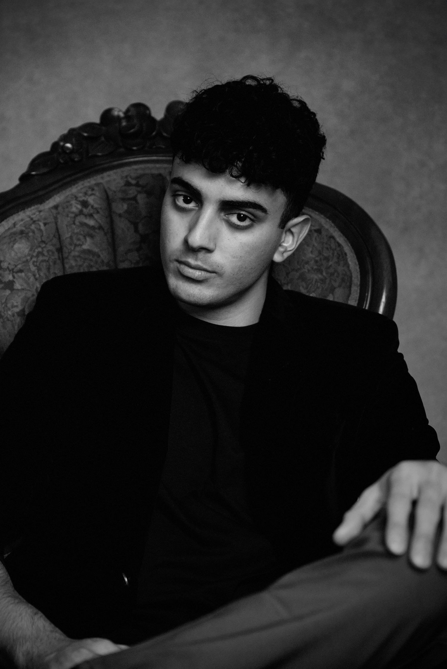Black and white portrait in vintage chair wearing dark clothing with classic styling.