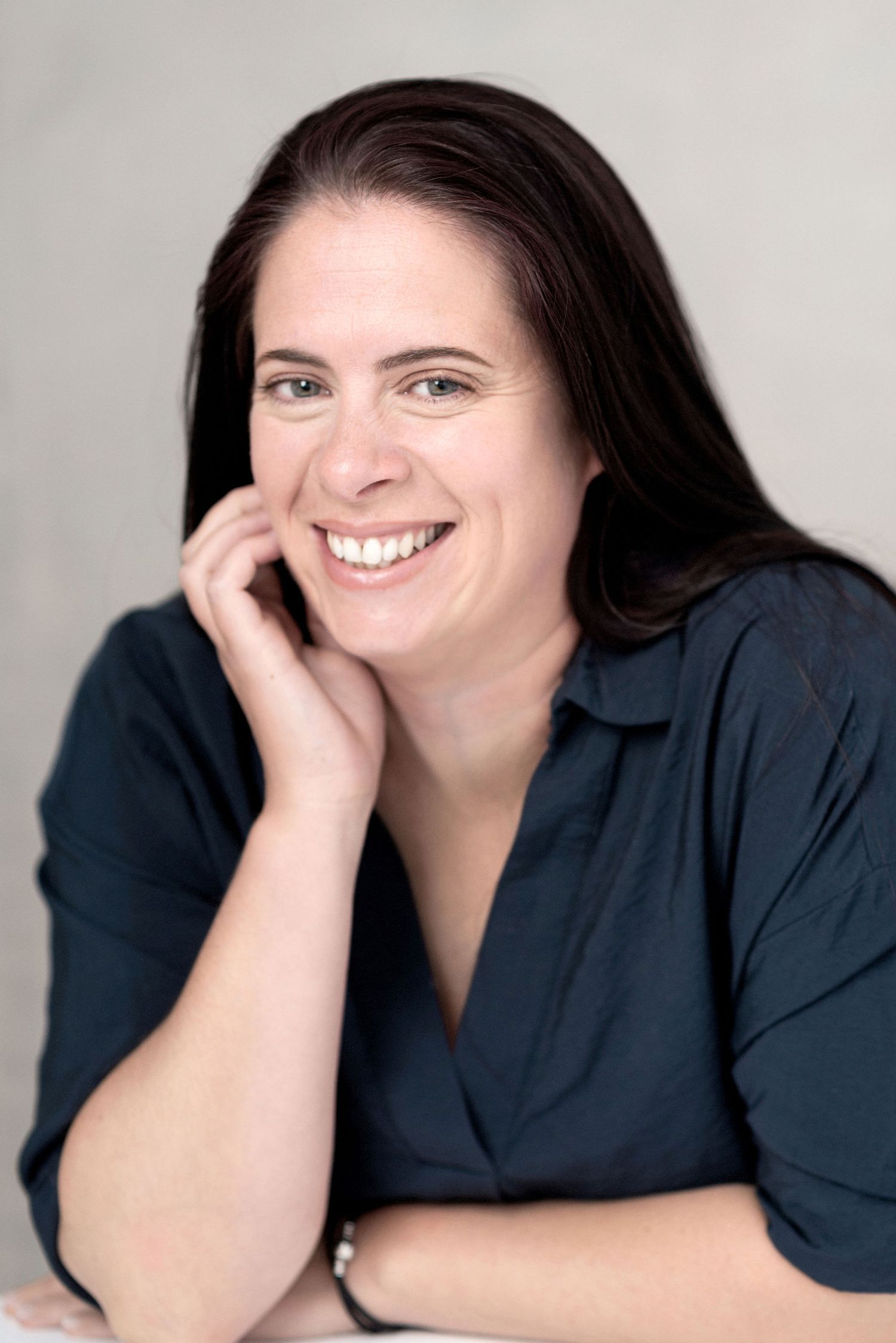 Studio headshot of person in navy top with natural smile against gray background.