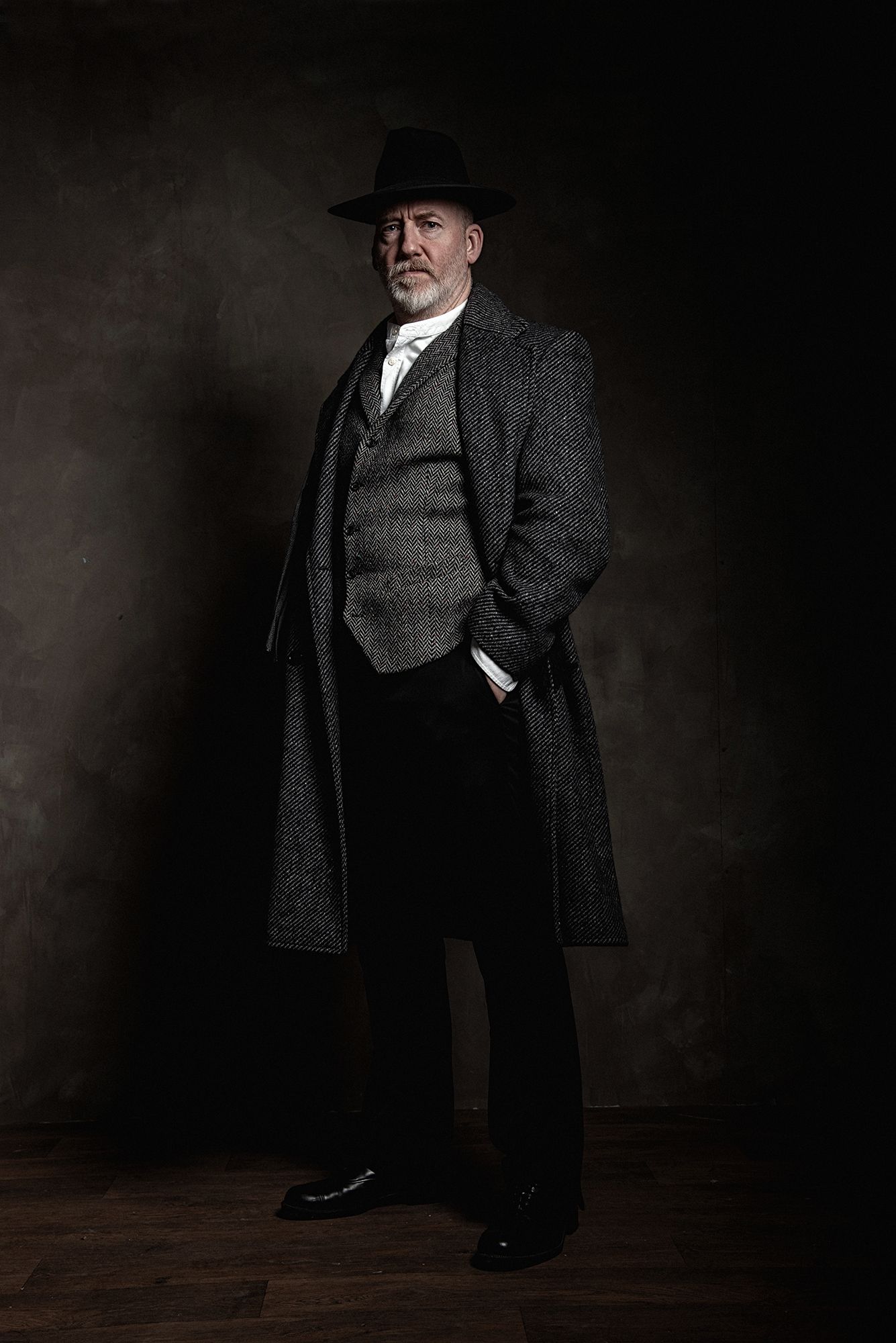 Dramatic portrait of person in vintage wool coat and hat against dark background.