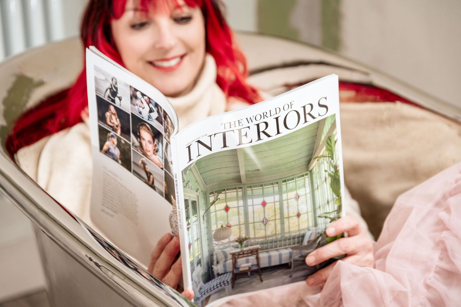Someone with bright red hair reads an interior design magazine while relaxing on a couch.