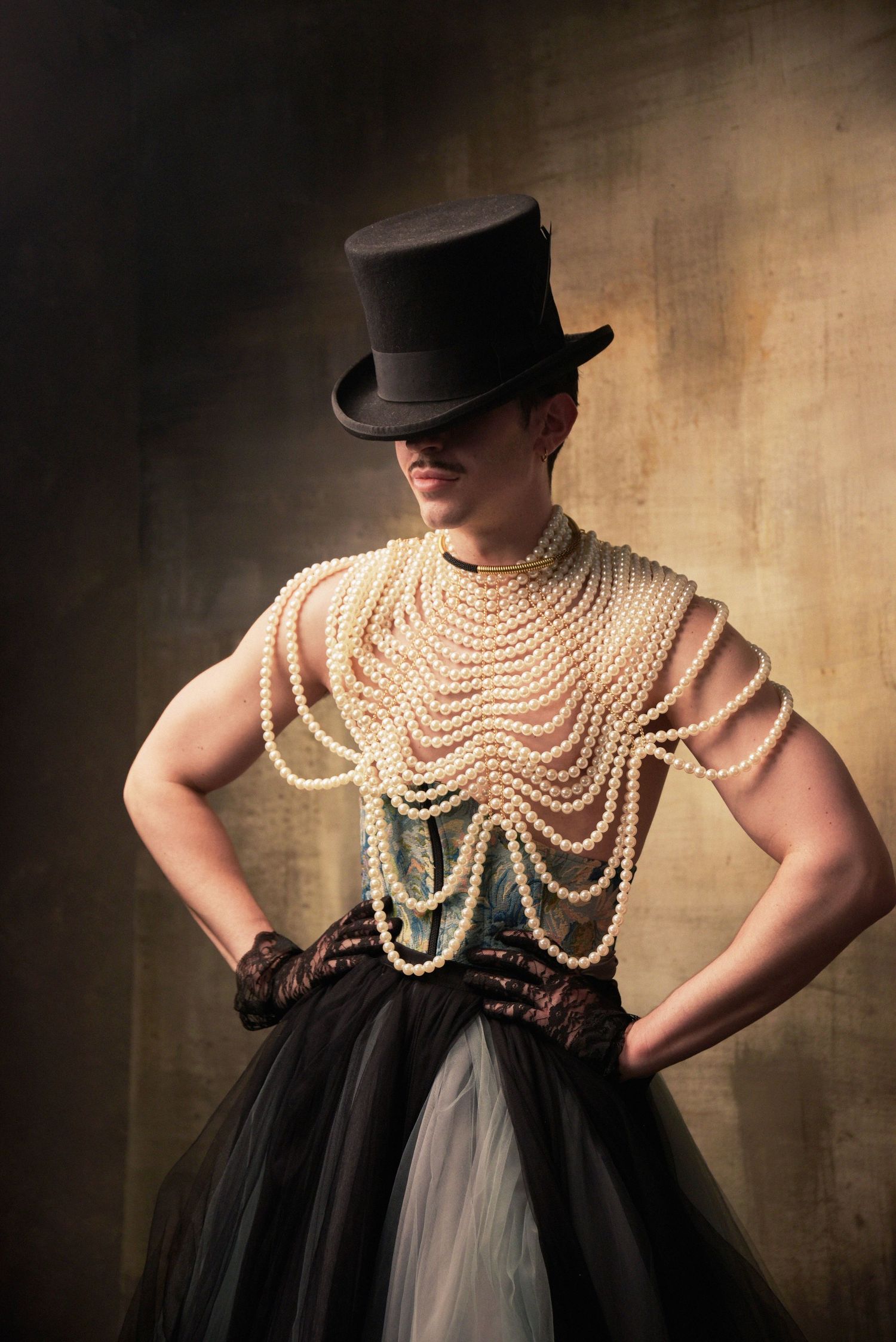Figure in top hat and pearl bodice with dramatic tulle skirt in moody lighting.