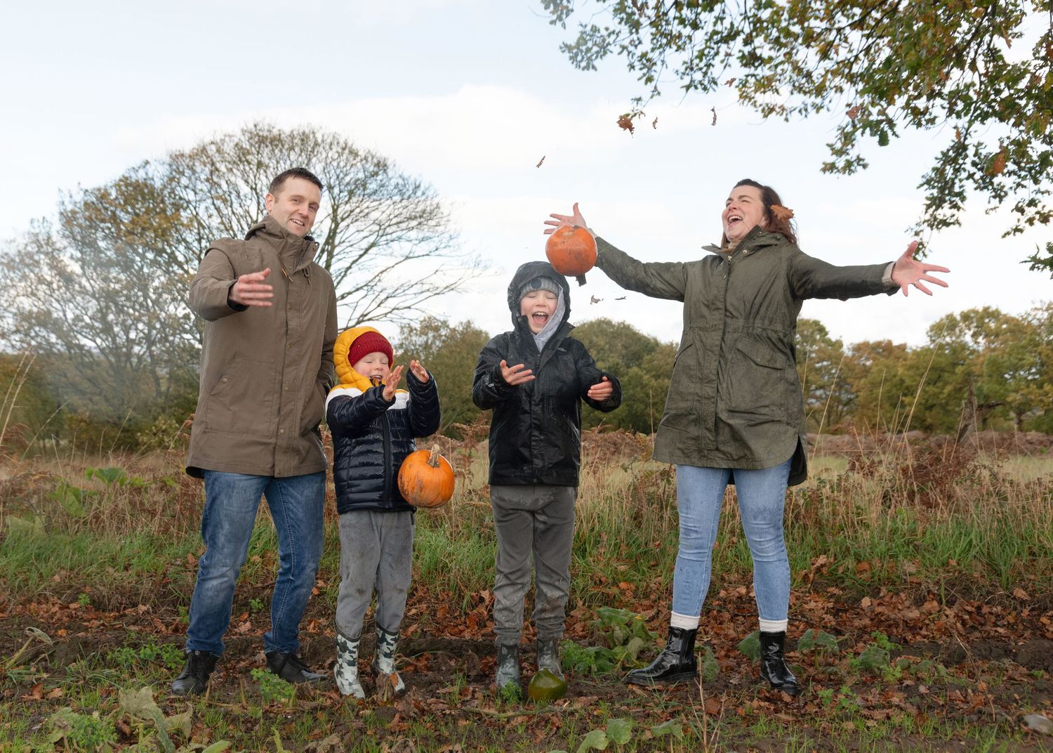 A family enjoying an autumn day outdoors in a field with fall foliage and trees in the background.