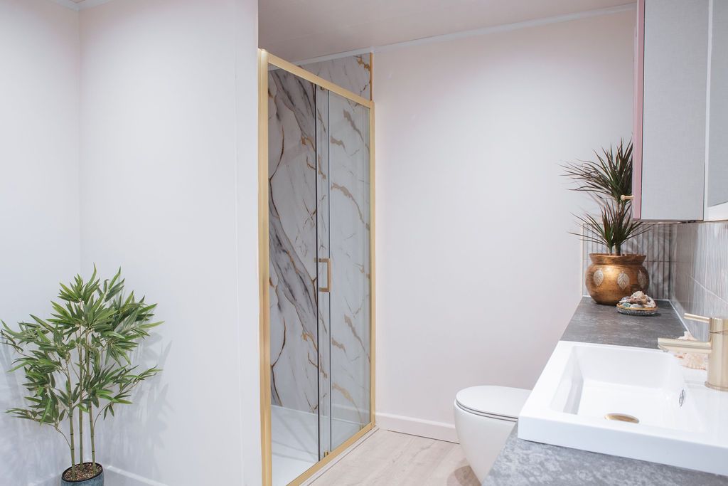 Modern bathroom interior with marble shower enclosure, white walls, potted plants and gold accents creating a spa-like atmosphere.