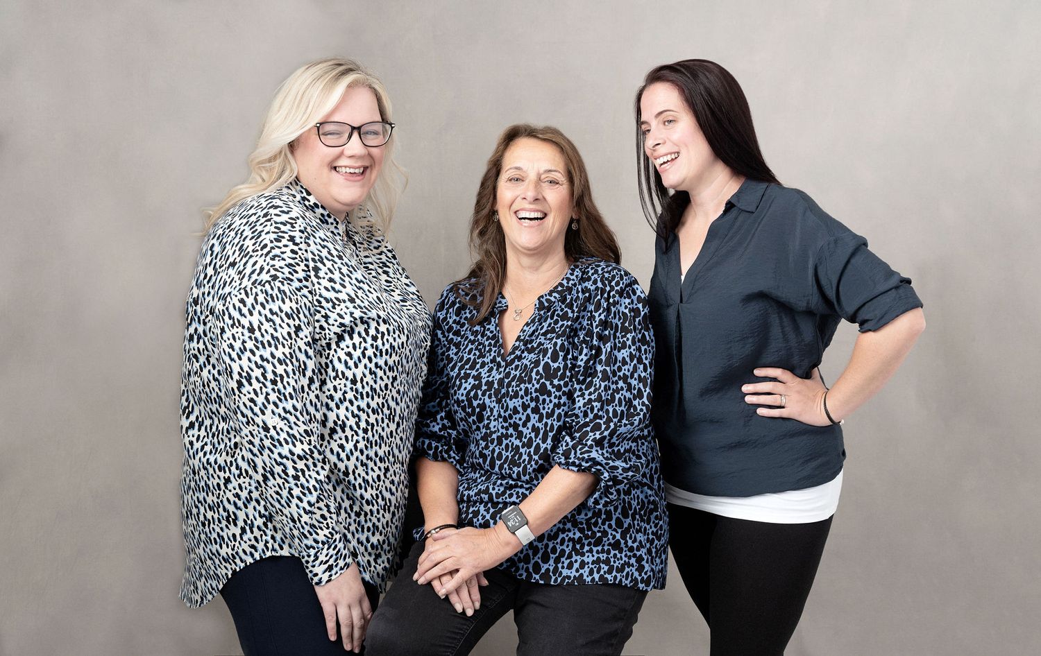 Candid studio shot of three colleagues sharing a joyful moment against neutral background.