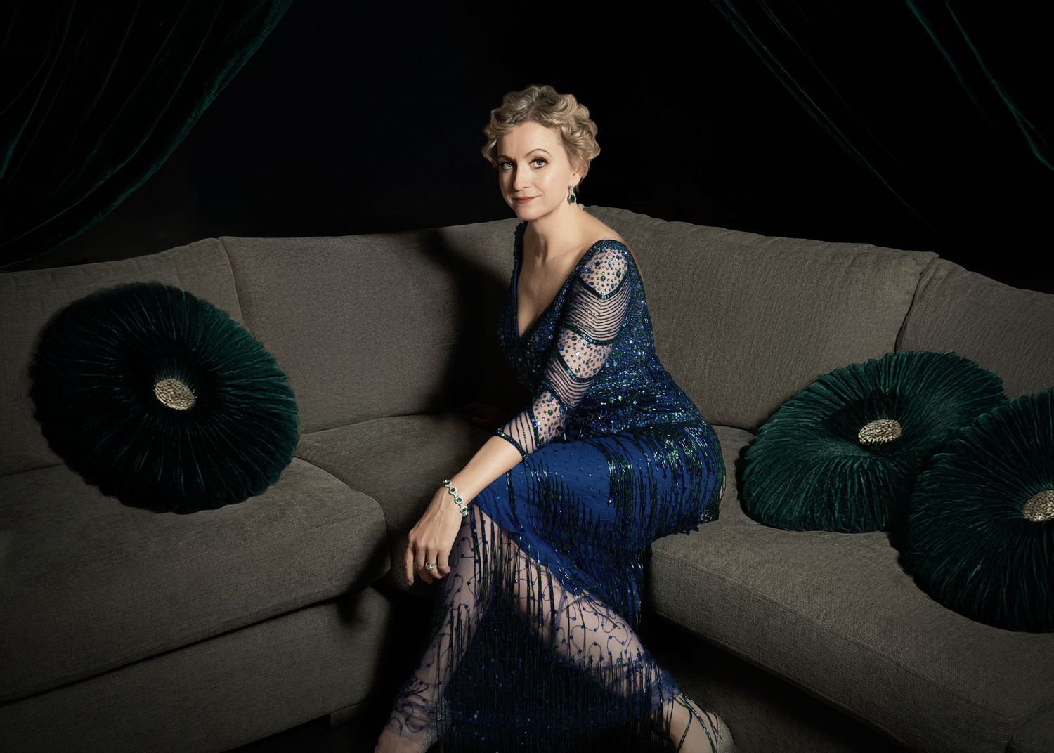 Sophisticated evening portrait in blue lace dress seated on grey couch with emerald pillows.
