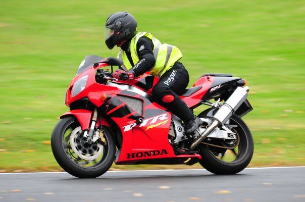 Rider in yellow vest and black helmet on a red Honda VFR motorcycle racing on a track.
