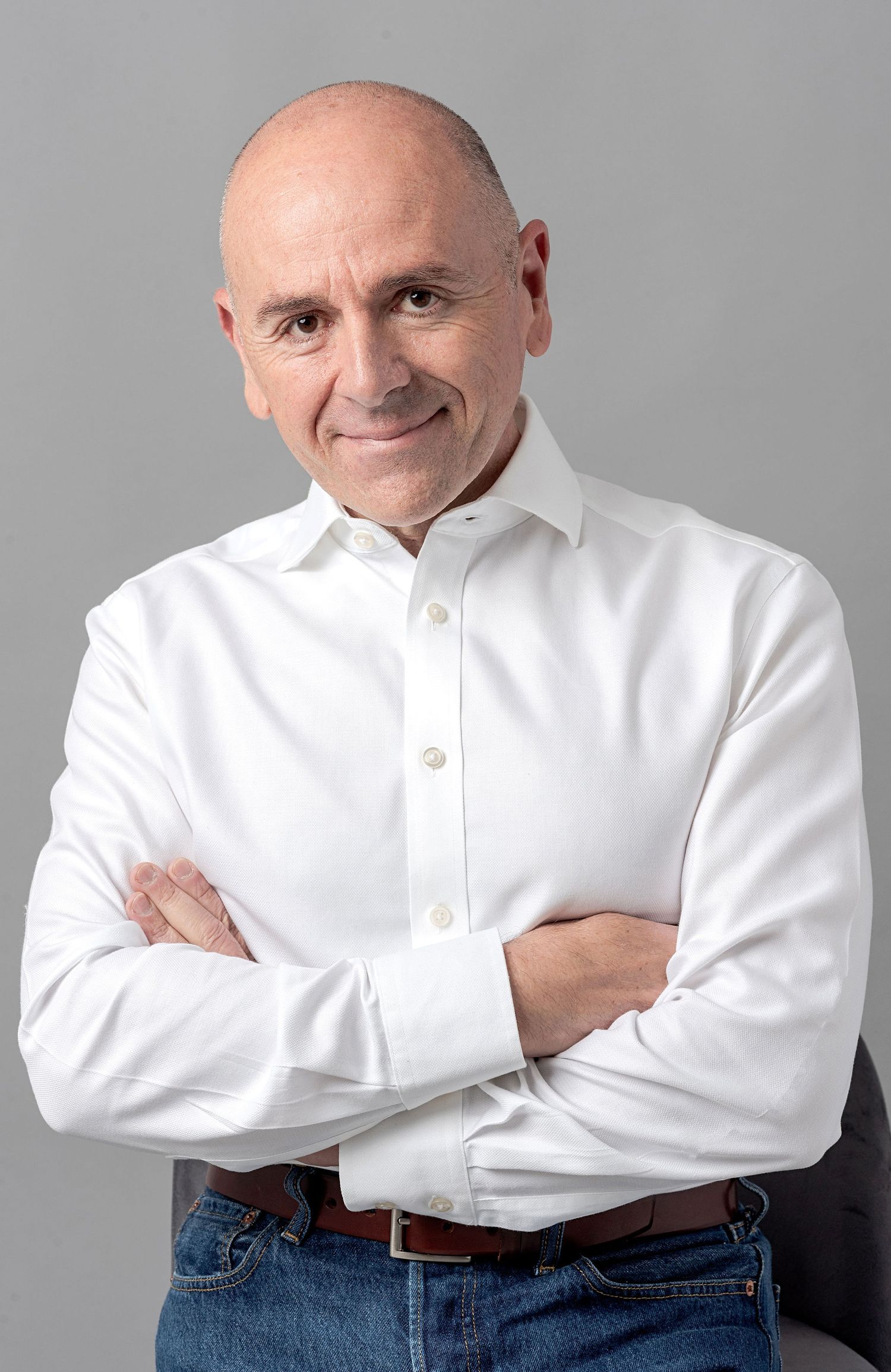 Professional headshot of a person in white shirt with arms crossed against grey background.
