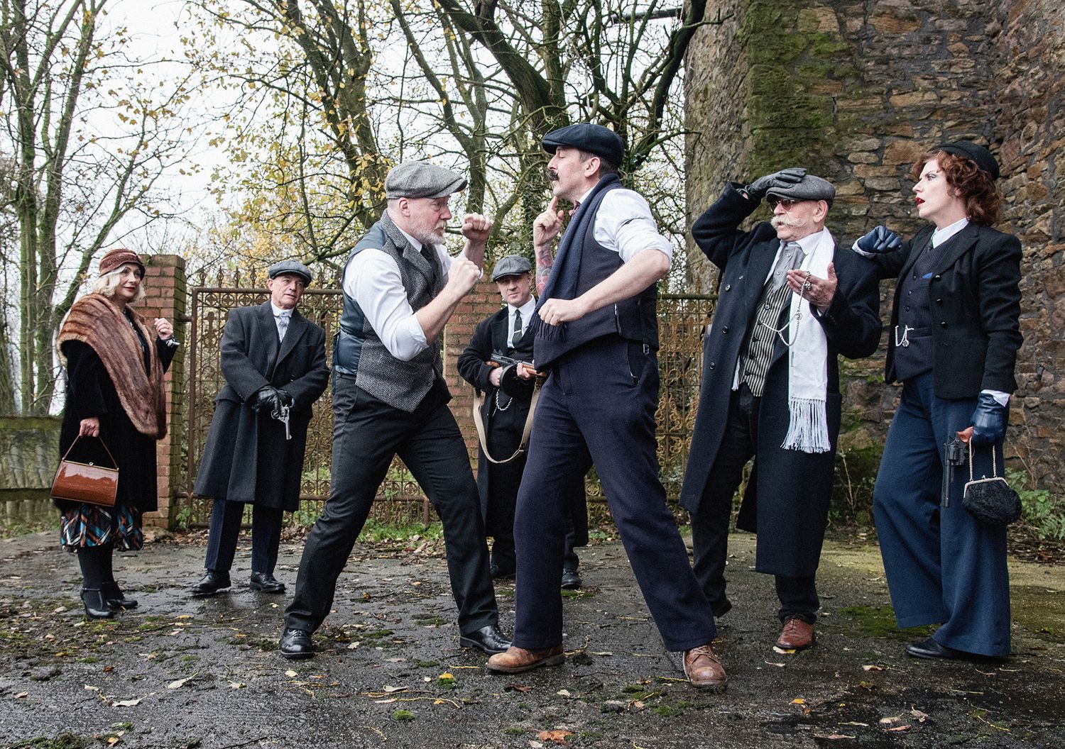 Group in vintage 1920s costumes acting out dramatic scene outdoors.