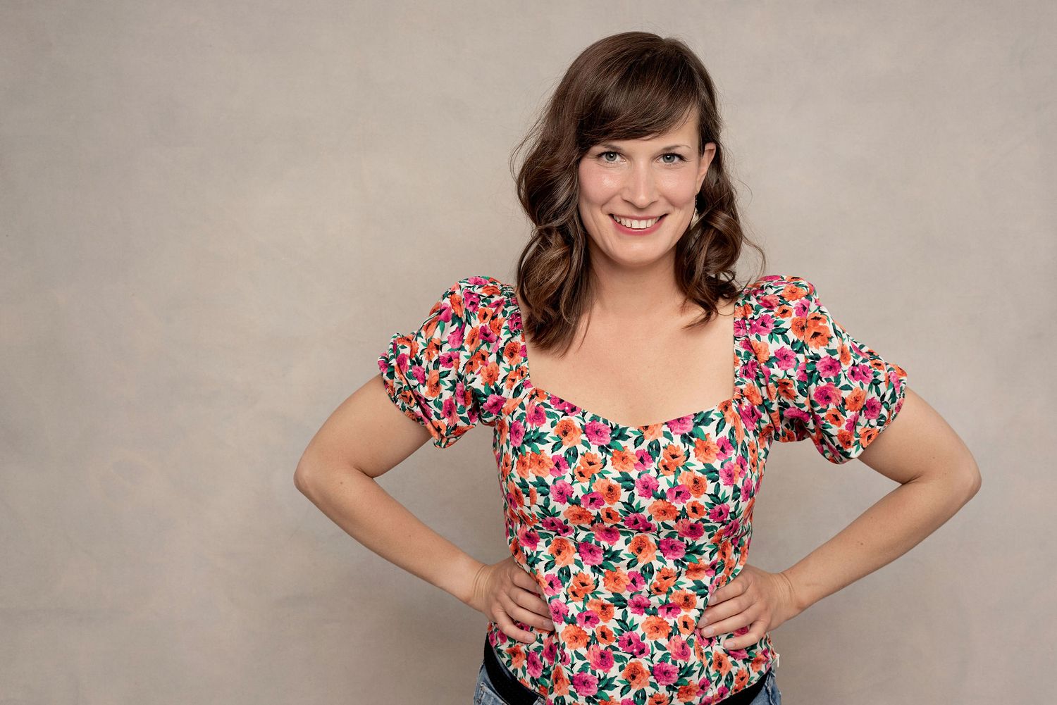 Studio photo showing bright floral print top and confident pose against beige backdrop.