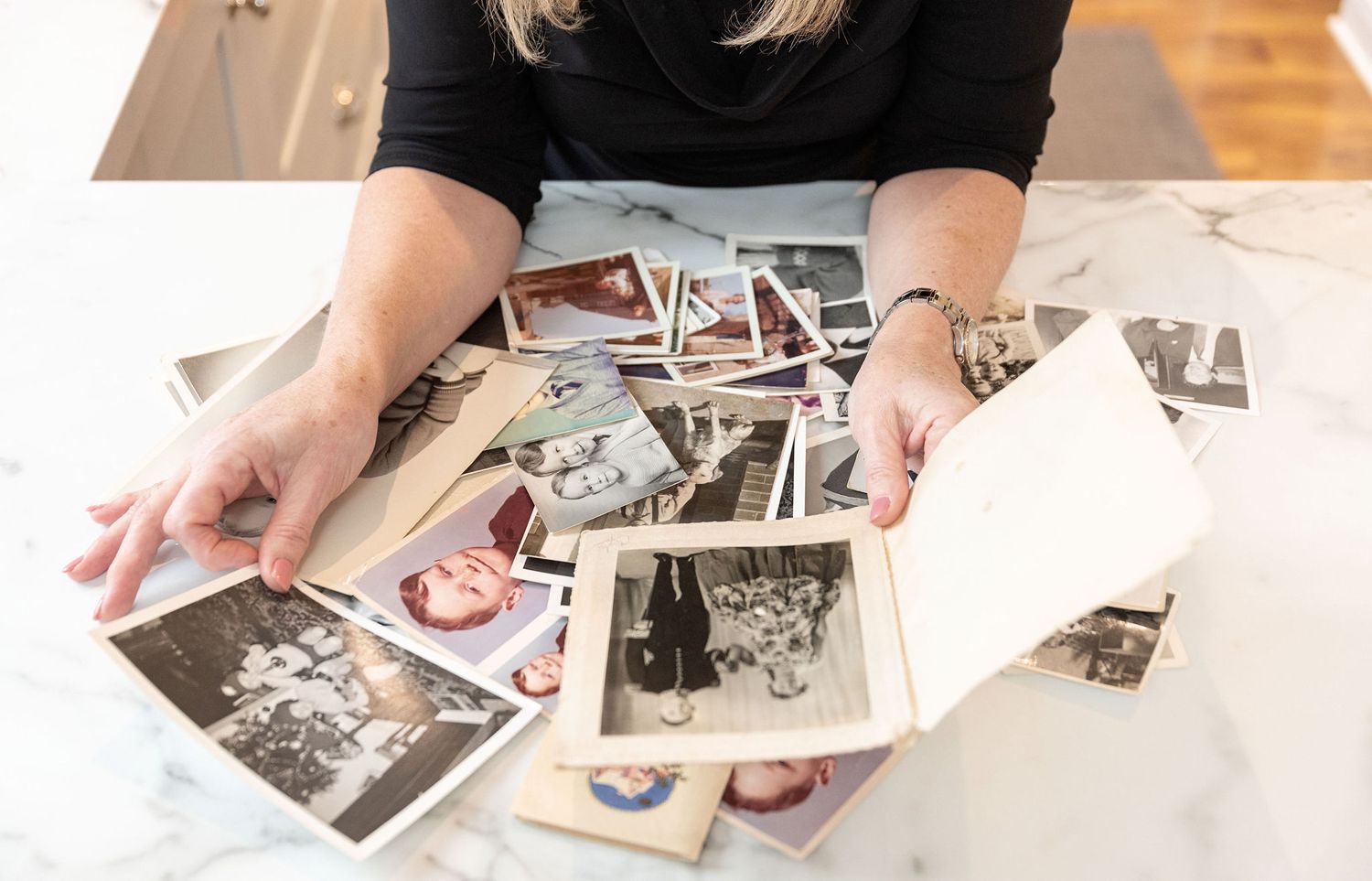 Hands sorting through vintage black and white photographs on a white table.