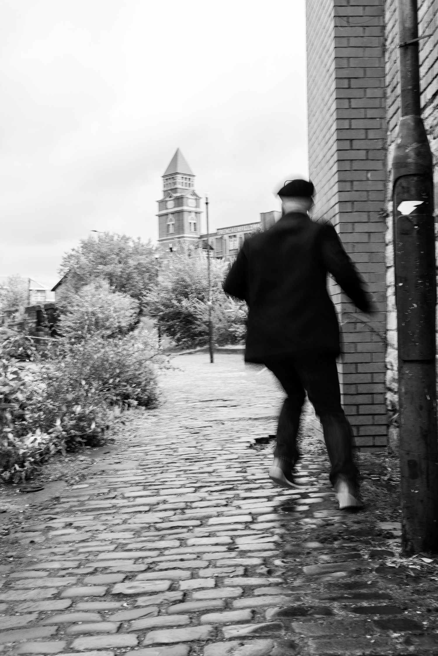 A person in dark clothing walks on a cobblestone path with a church tower visible in the background.