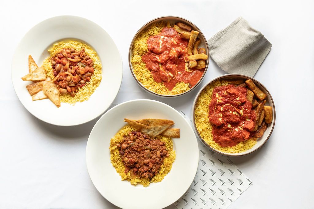Four bowls of yellow couscous topped with tomato sauce and crispy pita chips served on a white surface.