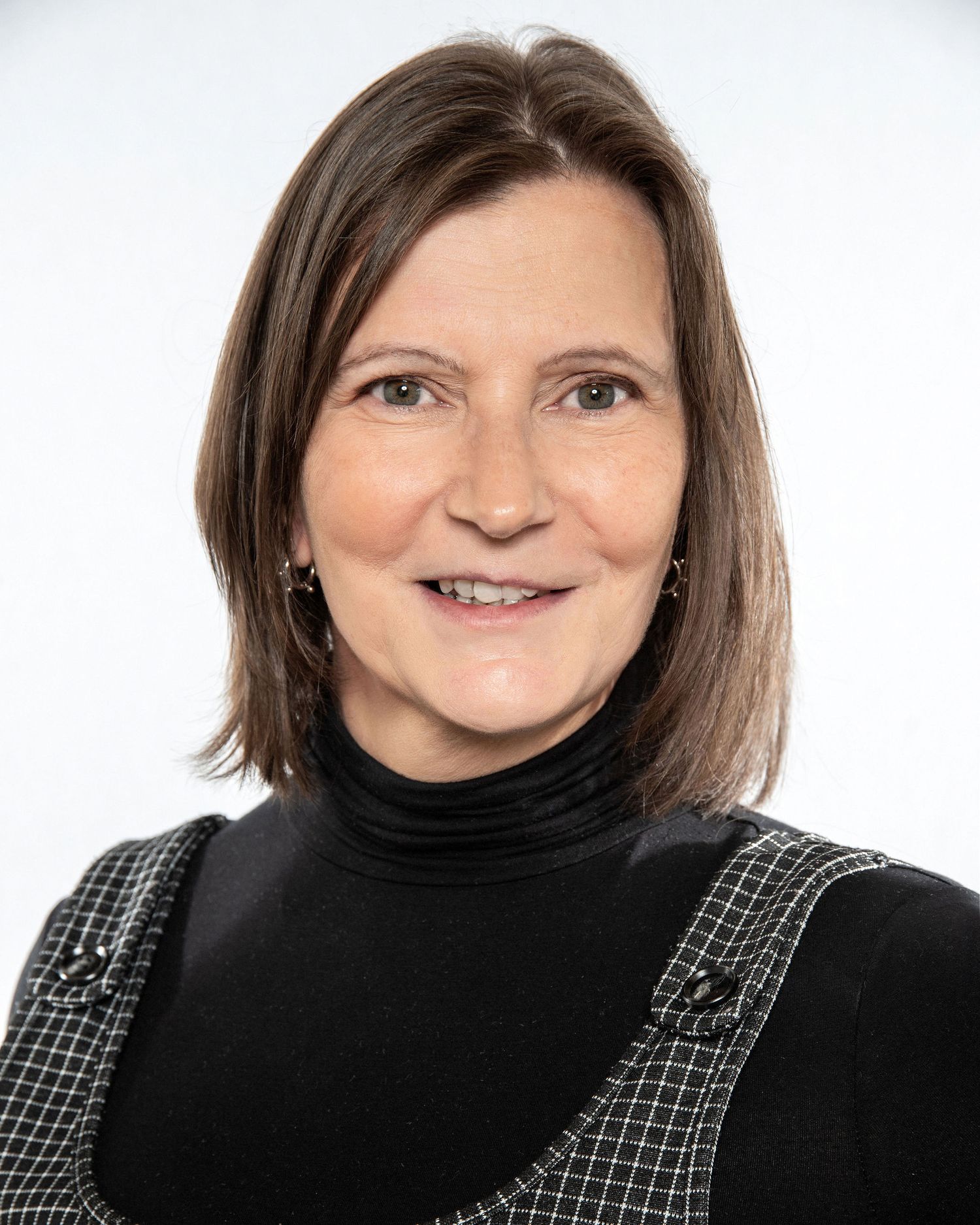 Professional headshot of person wearing black turtleneck and patterned jumper dress.