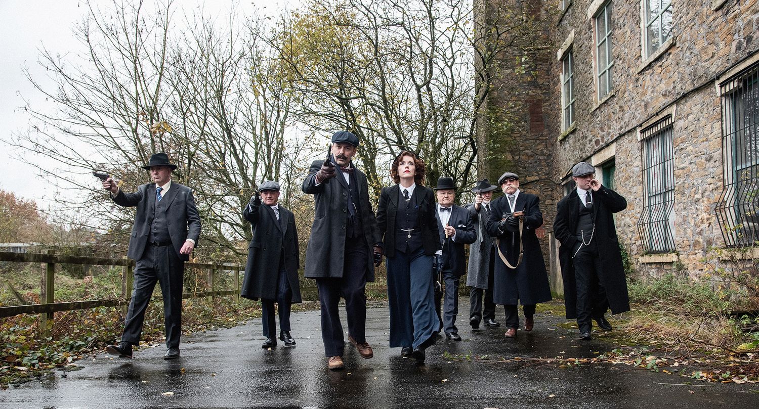 Group in period costumes standing outside historic brick building on rainy day.