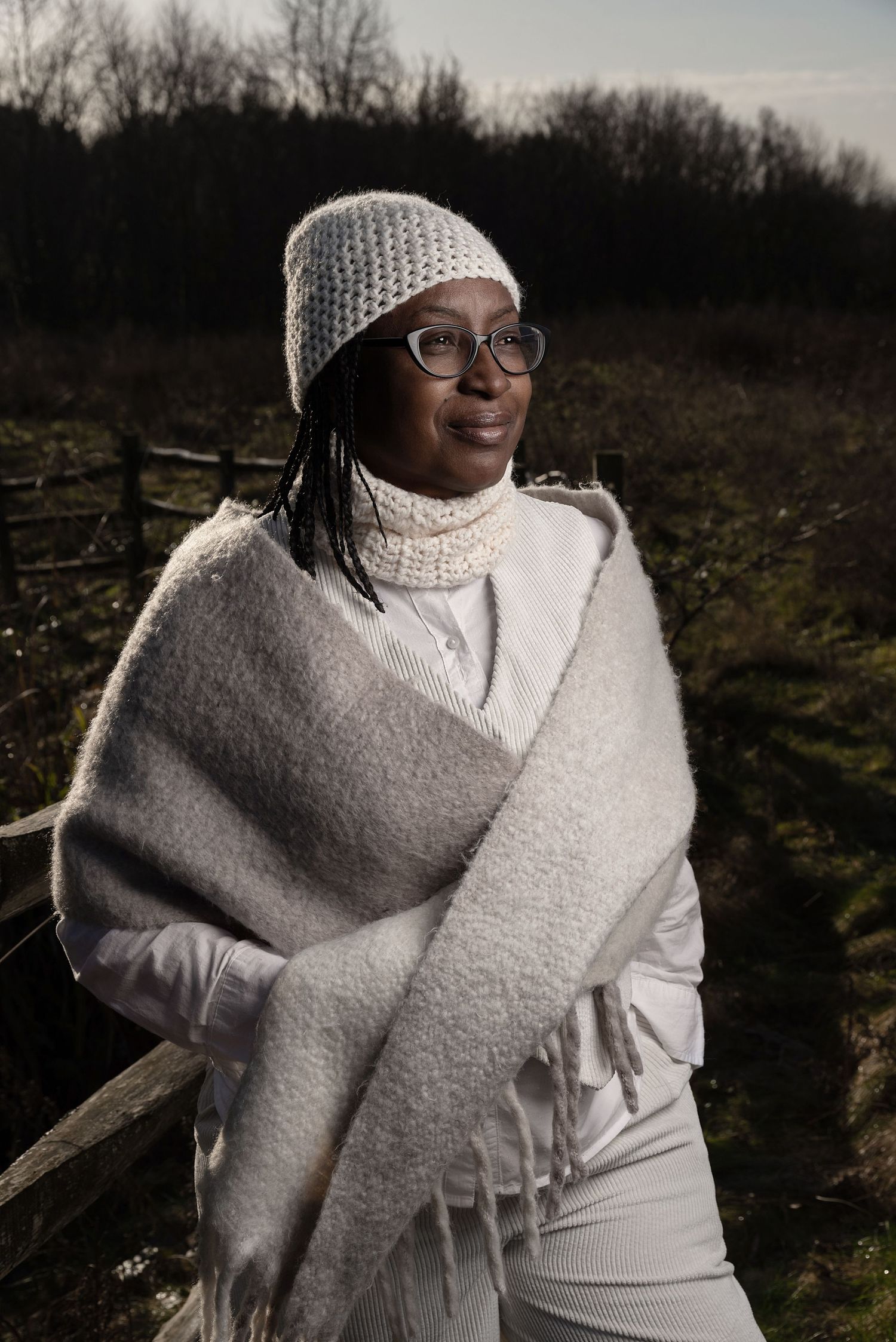 A person in a white knit hat and sweater gathers dried plants and grasses in a winter garden setting.