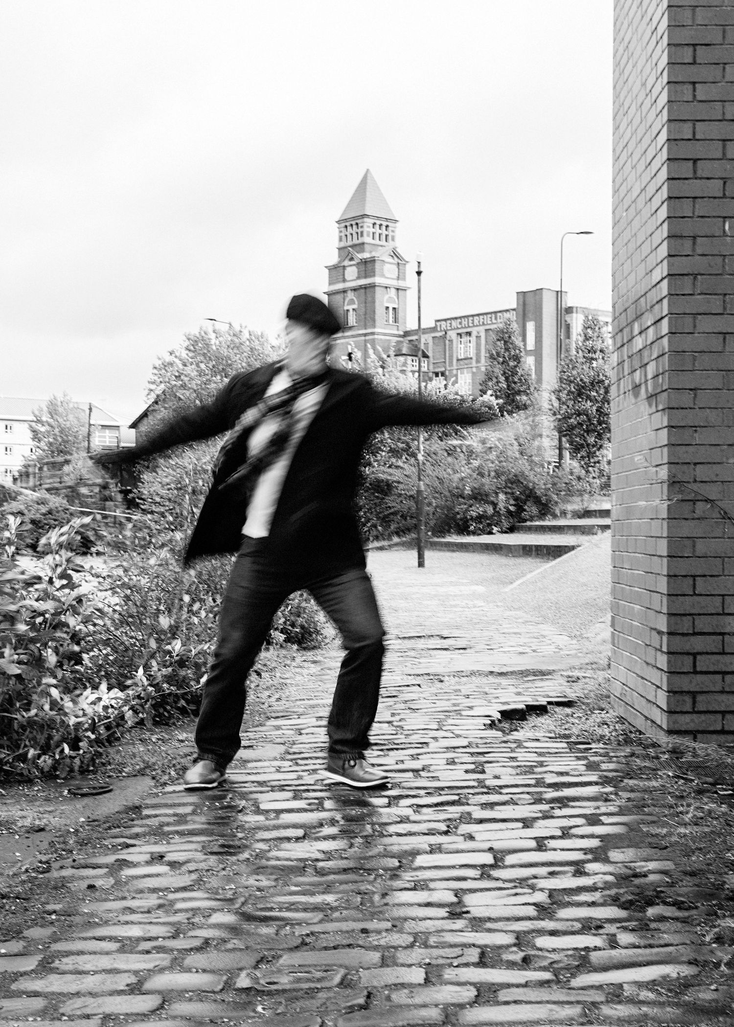 Black and white sequence shows a figure performing a cartwheel across a cobblestone path with church spires visible in background.