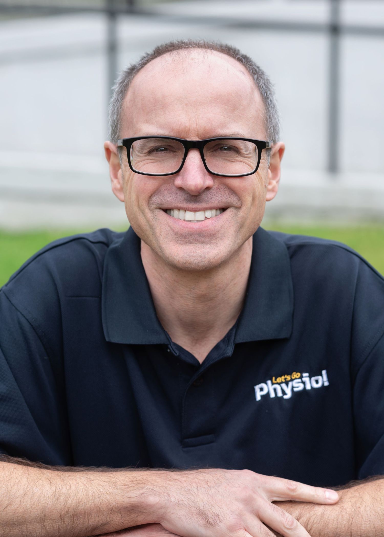A smiling person wearing glasses and a black polo shirt poses for a casual professional headshot against a light background.