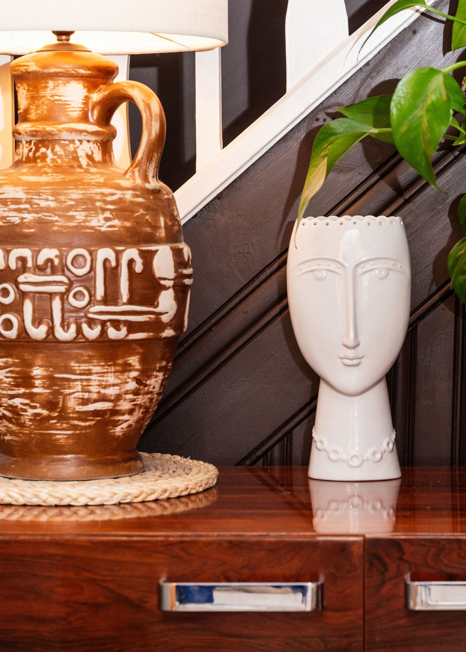 Decorative white ceramic face vases and brown pottery vessels arranged on wooden shelves against a dark wall.