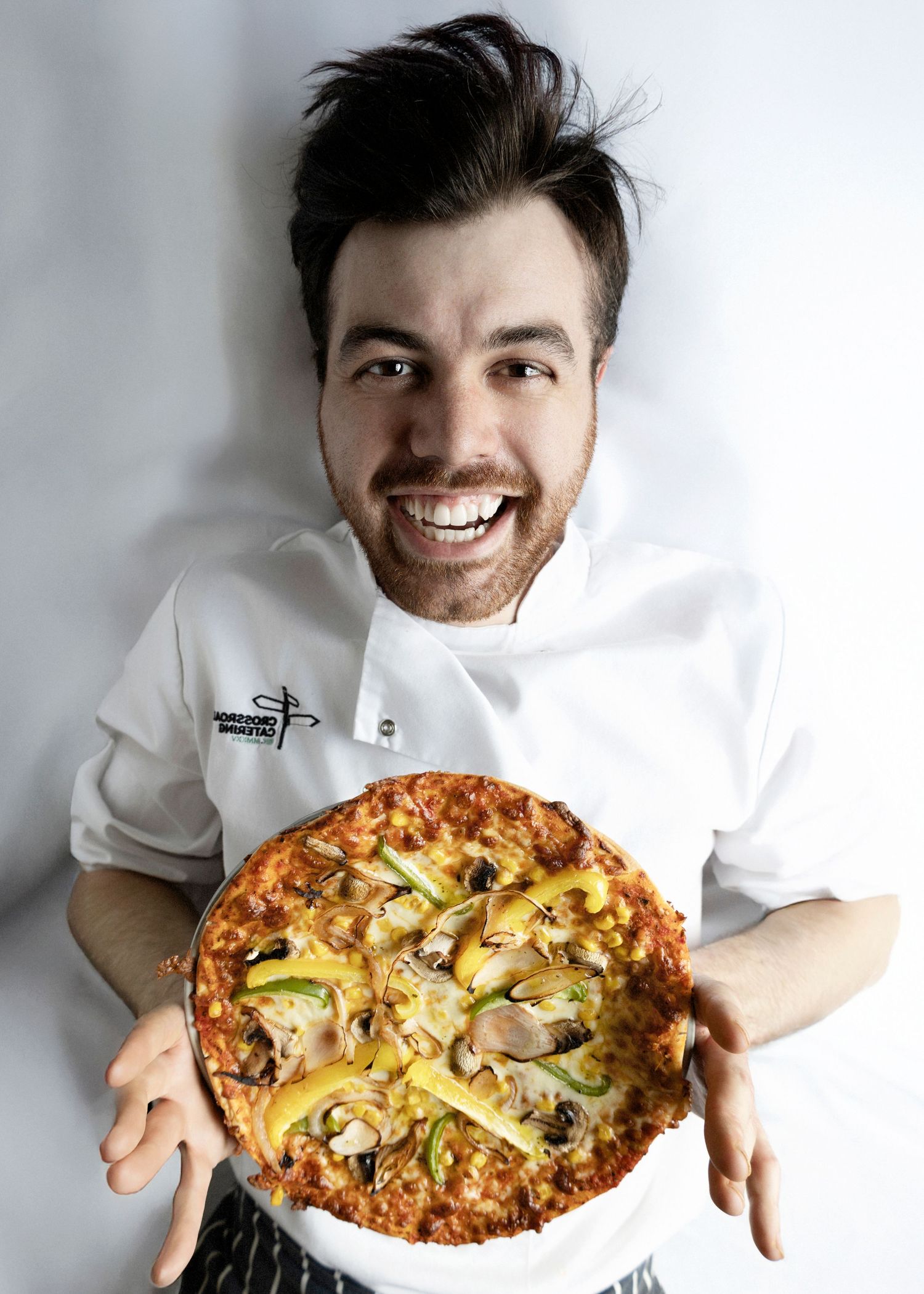 Chef shows off four homemade pizzas with various toppings on white plates against a light background.