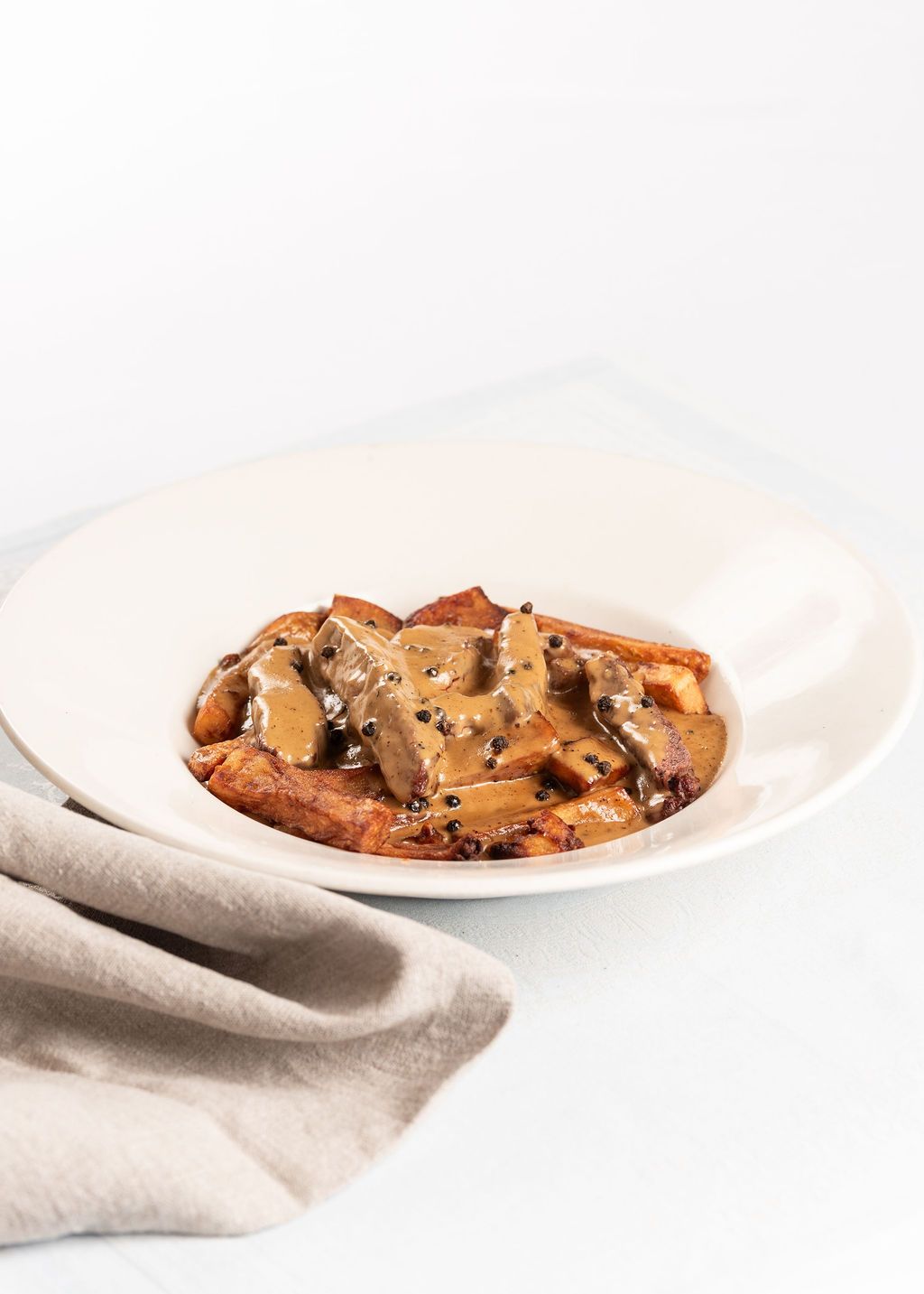 A white plate of sliced meat in rich mushroom gravy with black pepper, served over caramelized onions.