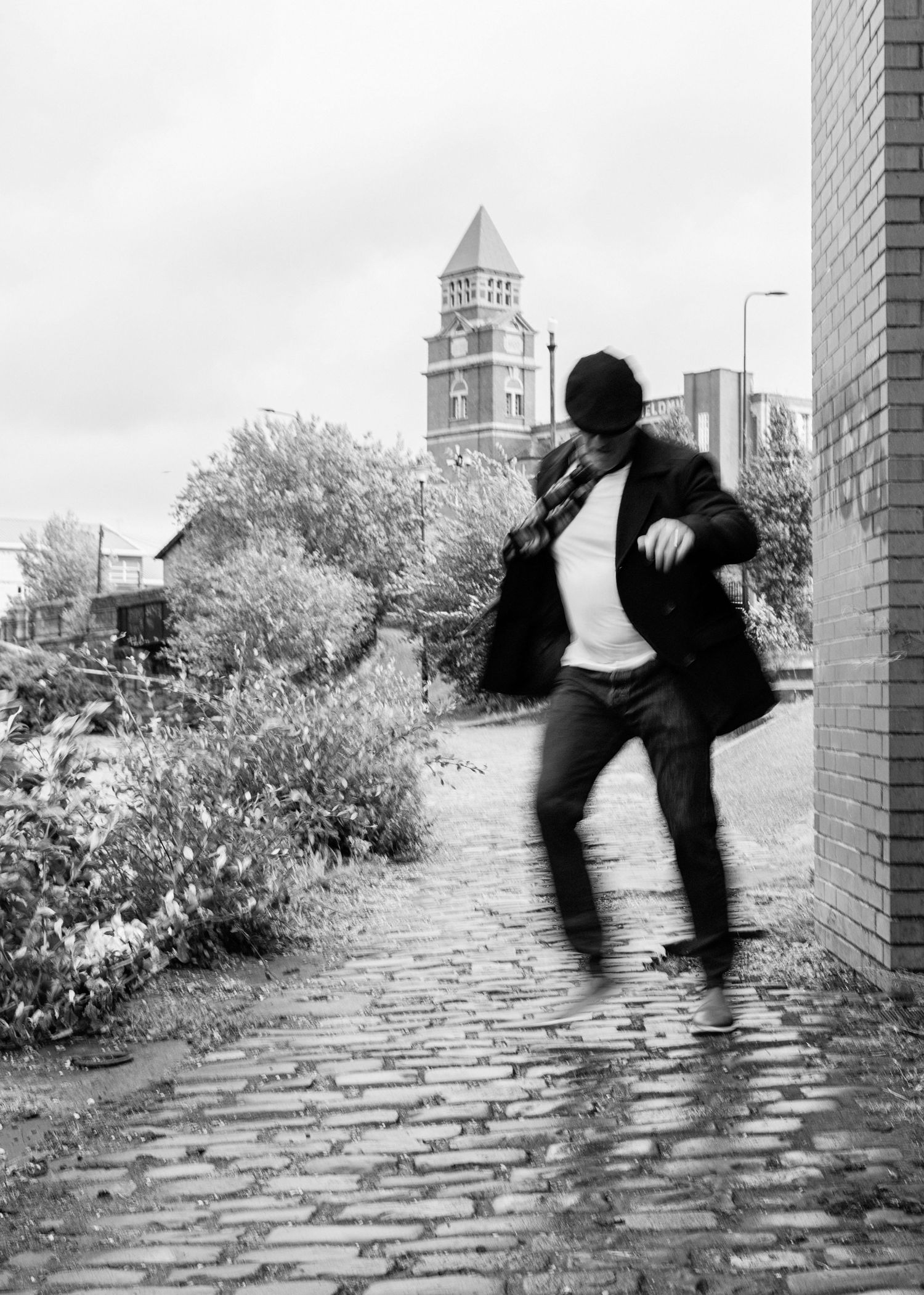 A sequence of four black and white photos showing a person climbing through a stone archway in an urban setting.