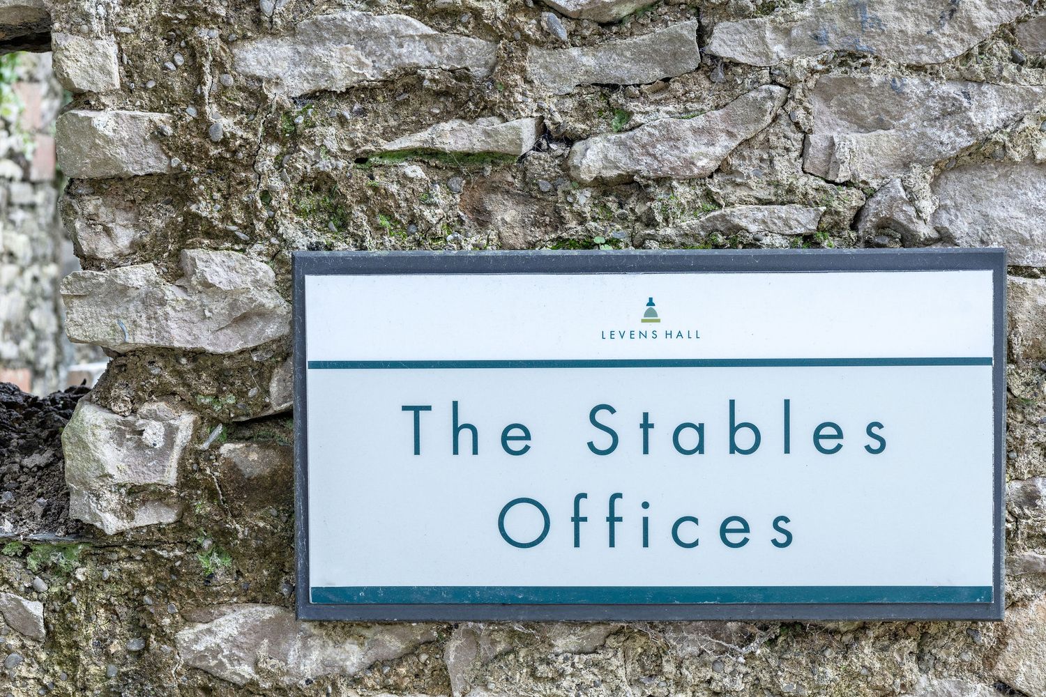 Blue and white office sign reading 'The Stables Offices' mounted on stone wall.