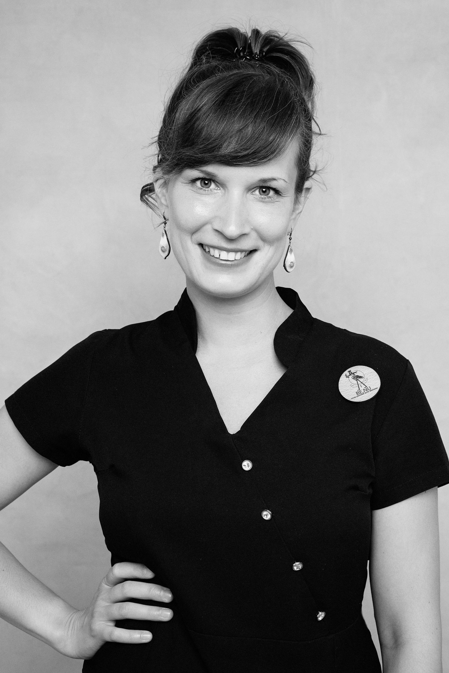 Professional headshot of someone in a black button-up shirt with a decorative pin smiling at the camera.