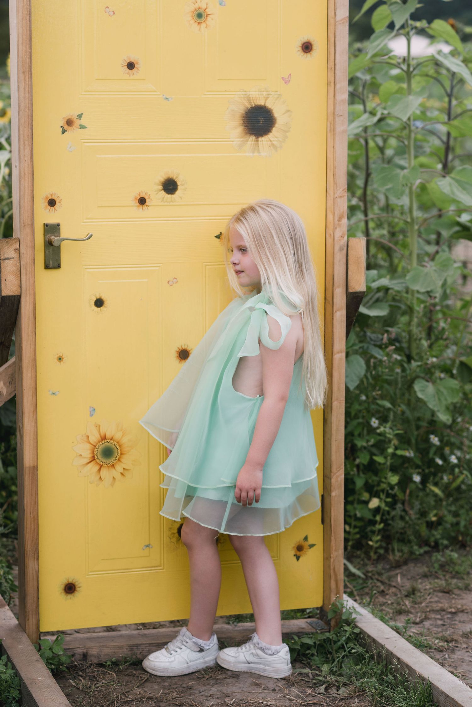 A series of photos showing a child in a mint green dress bending down to peek through holes in a yellow door.