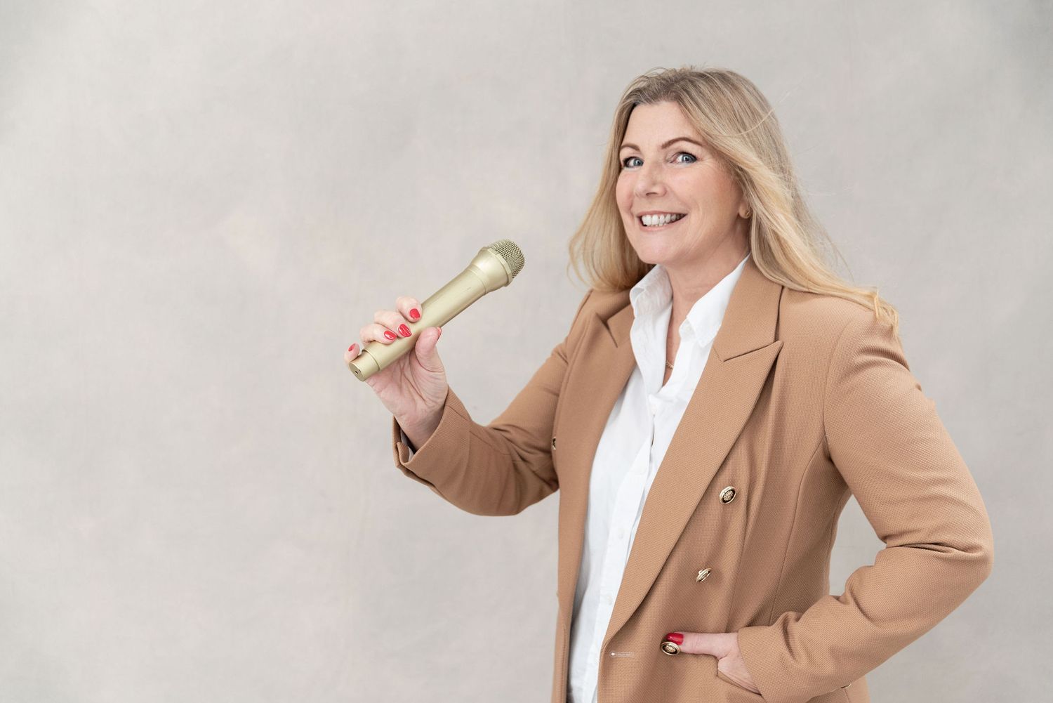 Person in business attire holding a gold microphone against a neutral background.