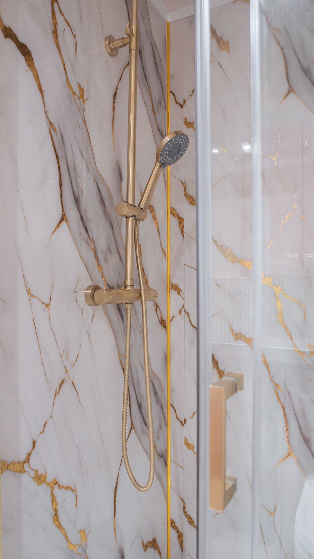 Modern bathroom shower enclosure with white and gold marble-effect walls and glass panels.