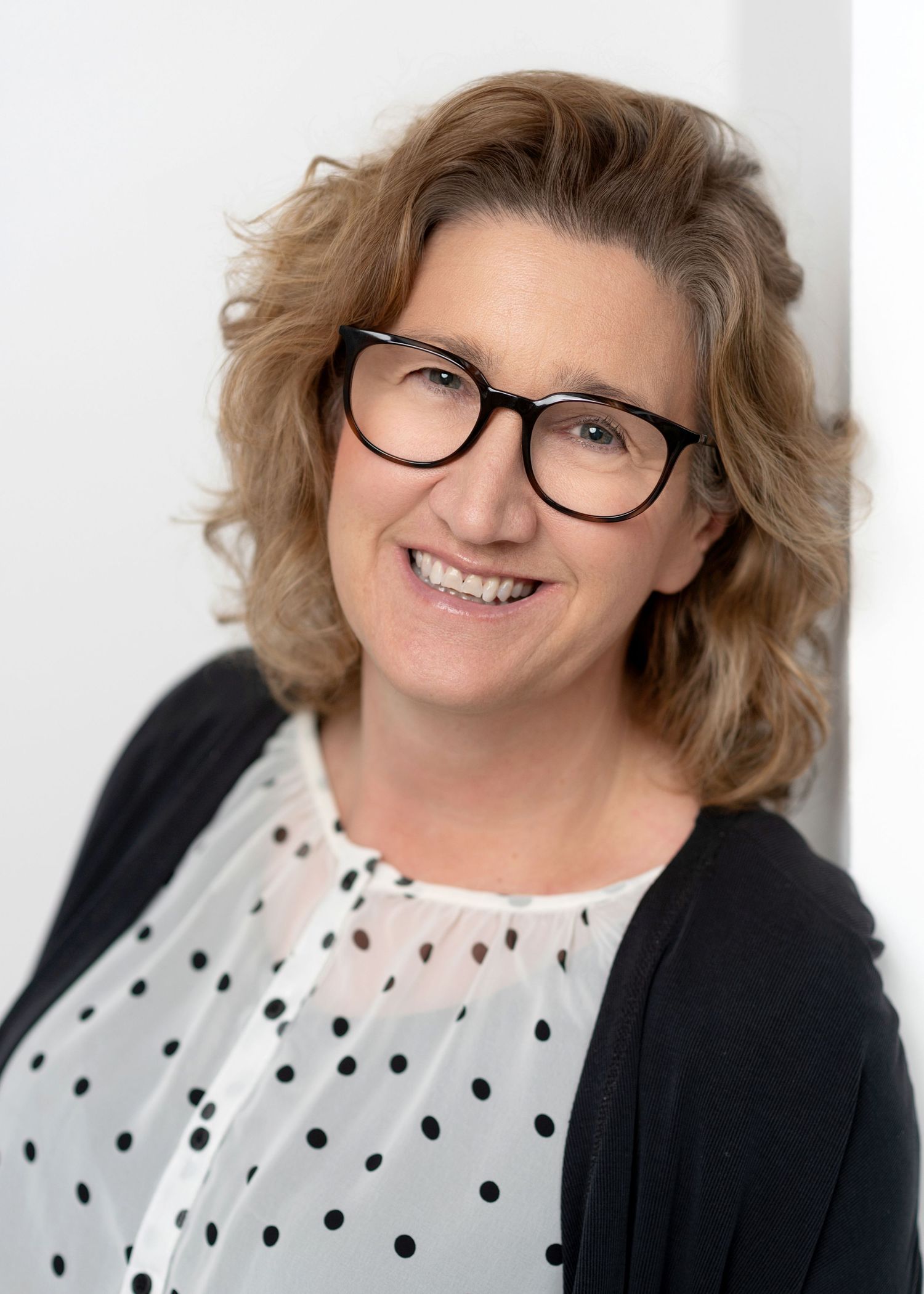 Professional headshot of woman in polka dot top and black cardigan against white background.