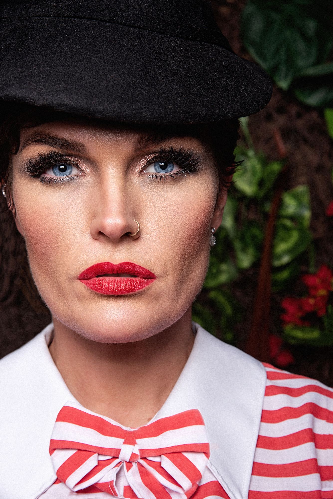 Close-up portrait featuring red lipstick, black hat, and striped bow tie accent.