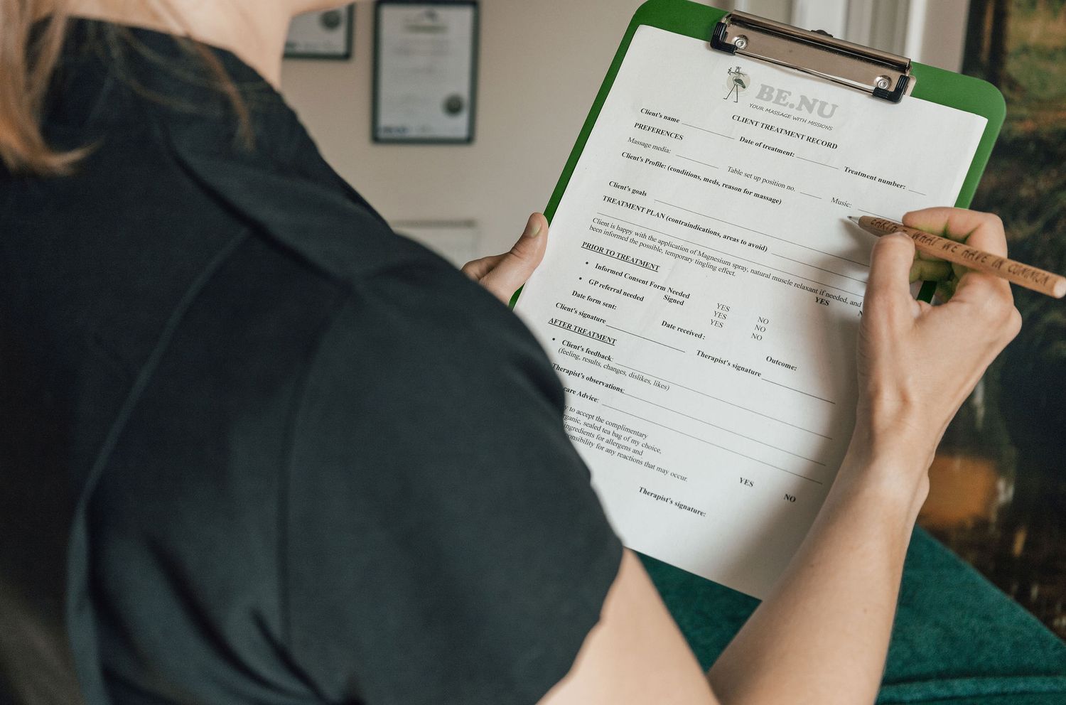 Someone filling out a client intake form on a green clipboard.