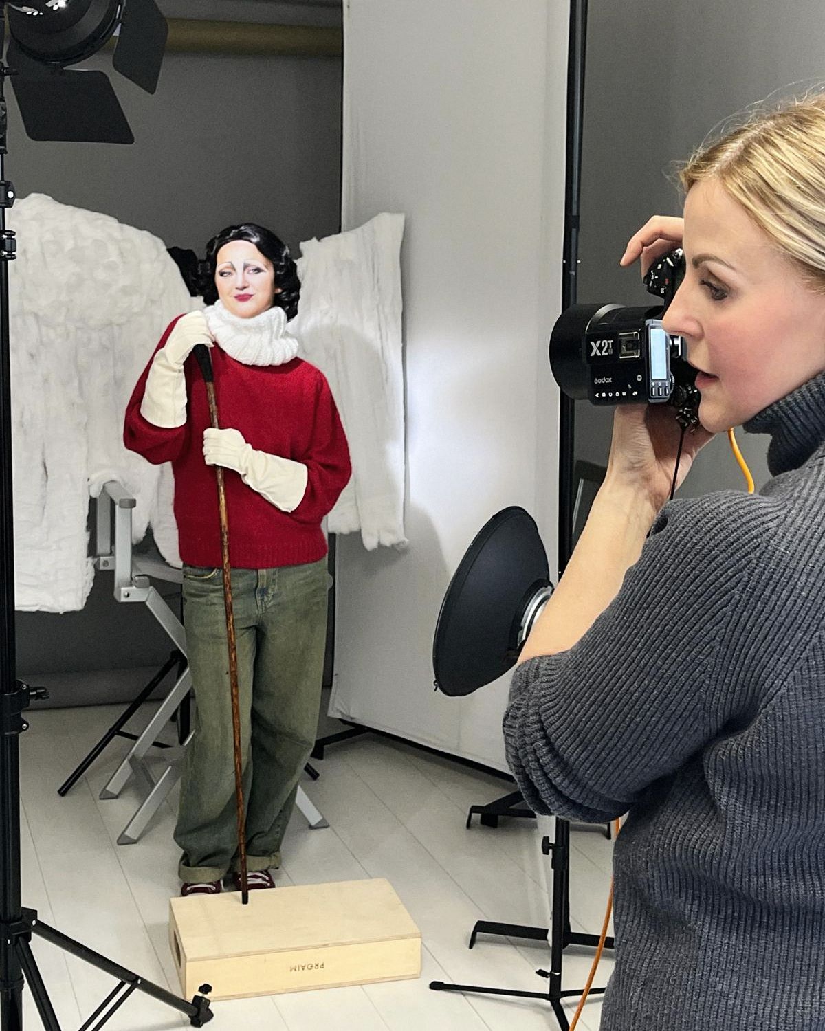 Fashion photography session with model posed on wooden block against white backdrop.