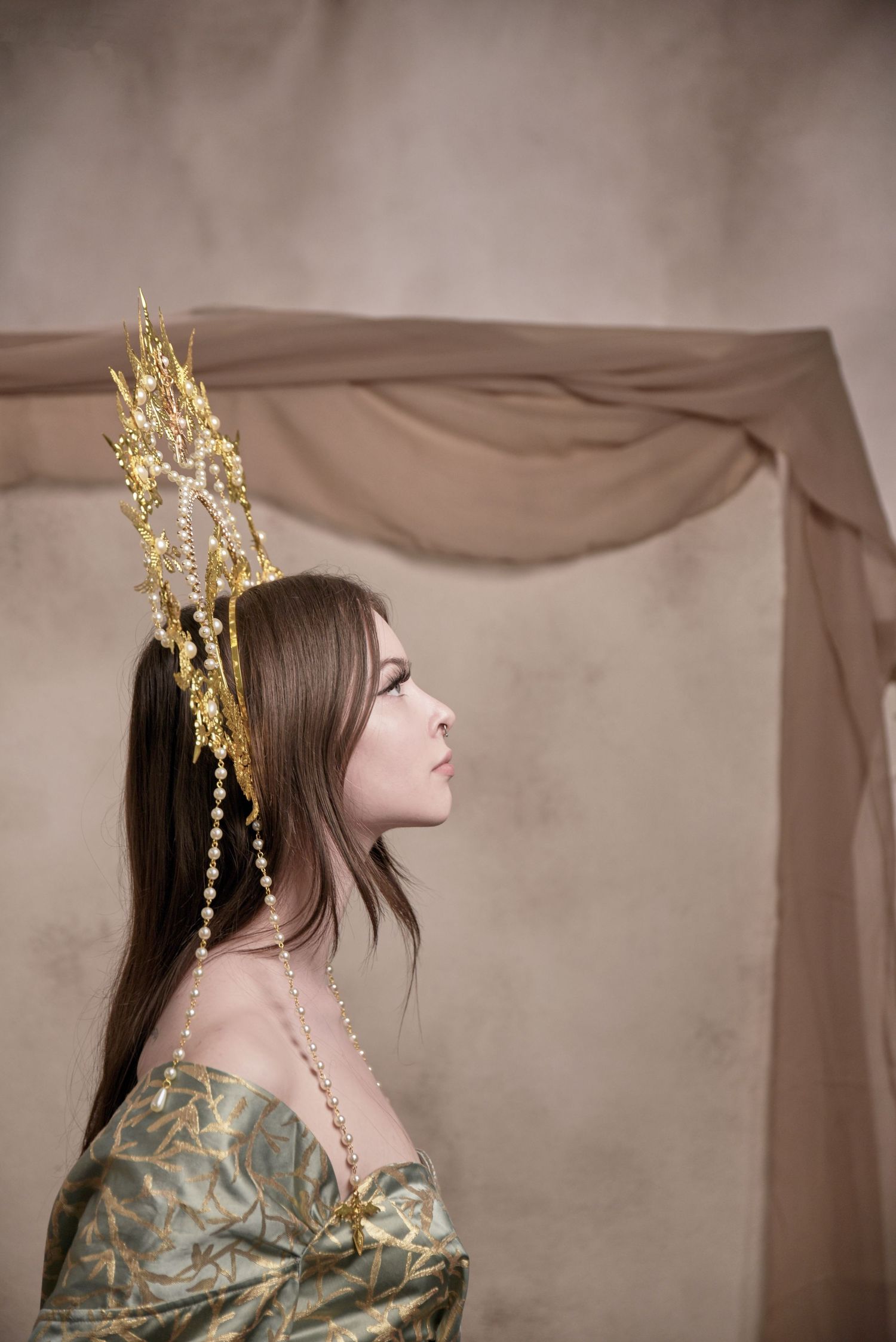 Side profile with ornate golden crown and pearls wearing vintage-inspired gown.