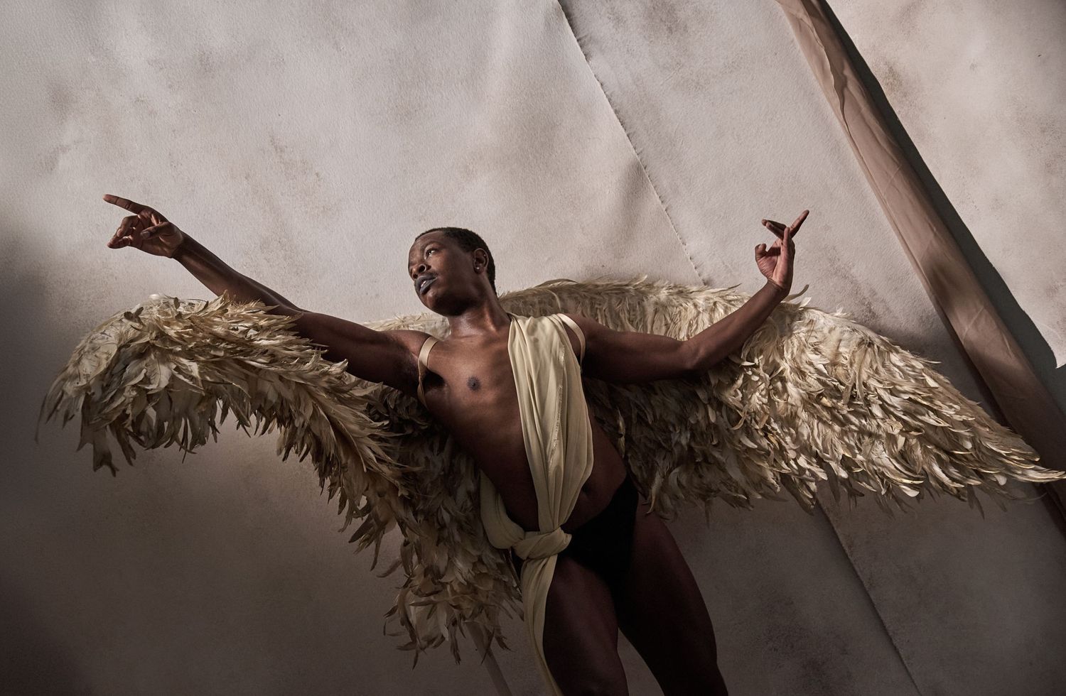 Artistic portrait of performer with dramatic feathered wings against fabric backdrop.