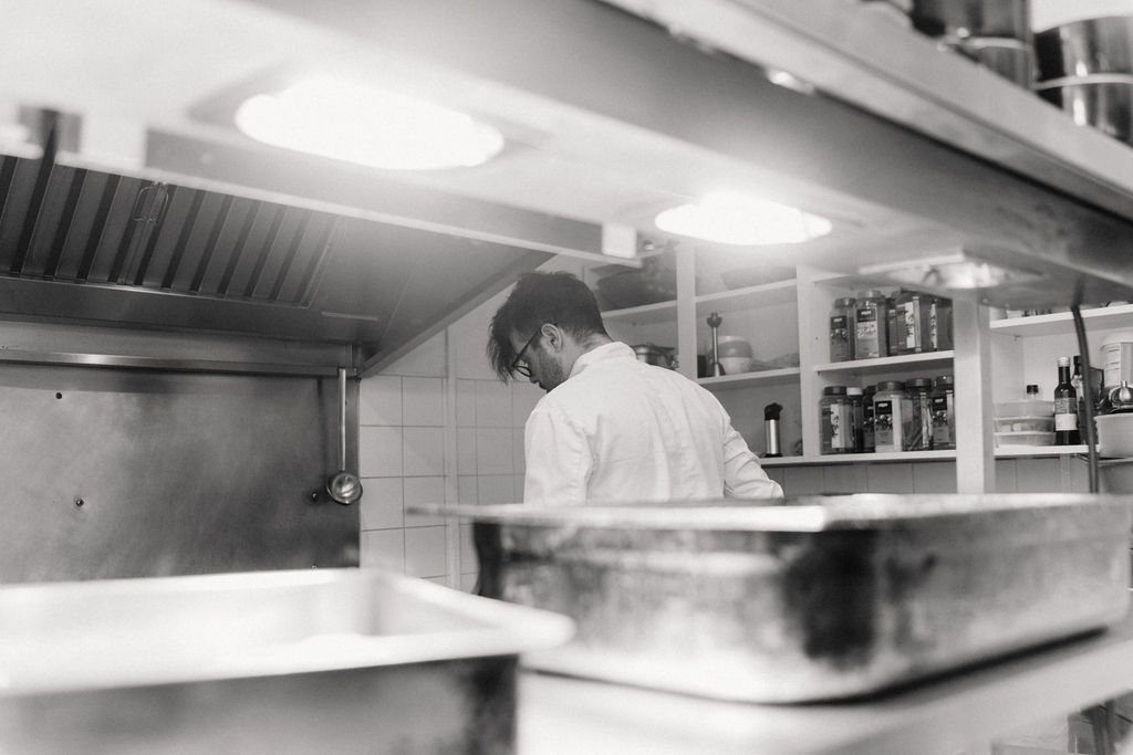 Black and white photo of a chef working in a professional restaurant kitchen with stainless steel equipment.