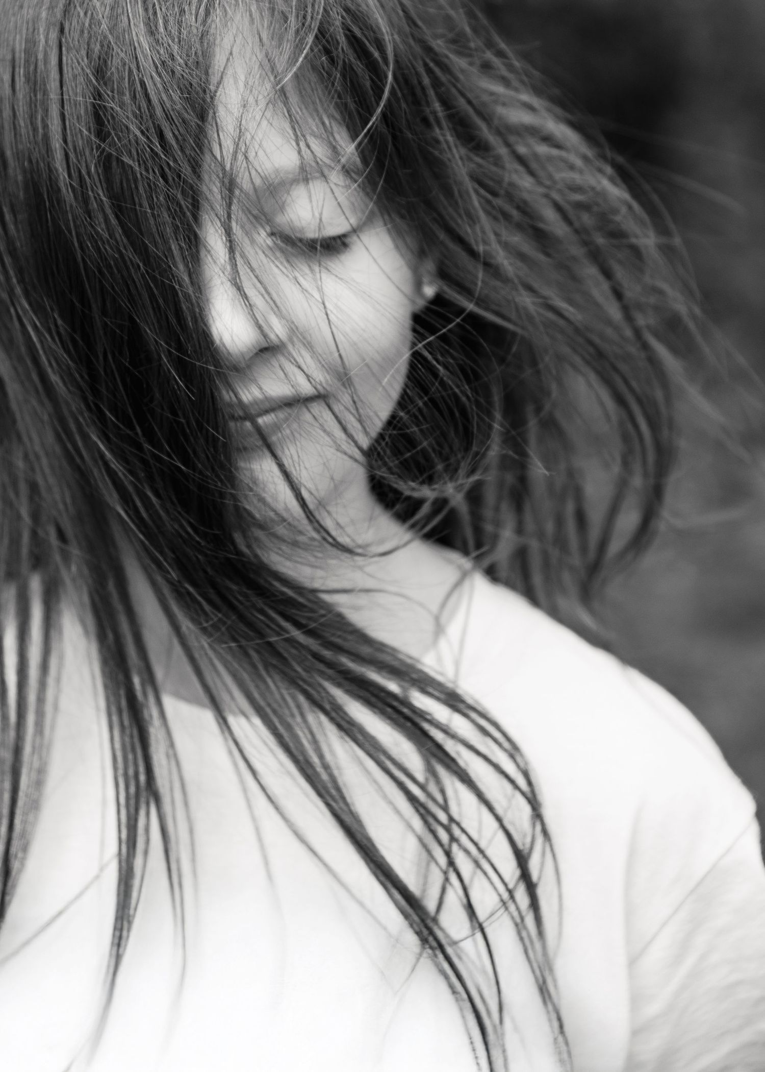 Black and white portrait of a young woman with windswept hair, eyes closed, wearing a white top.
