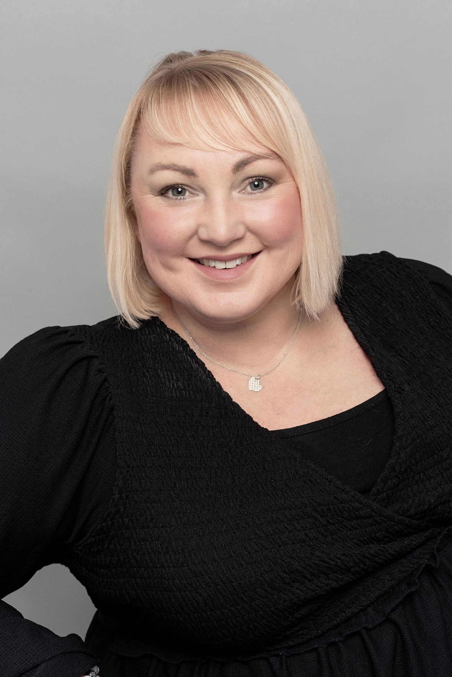 Professional headshot of a person wearing a black top against a grey background.