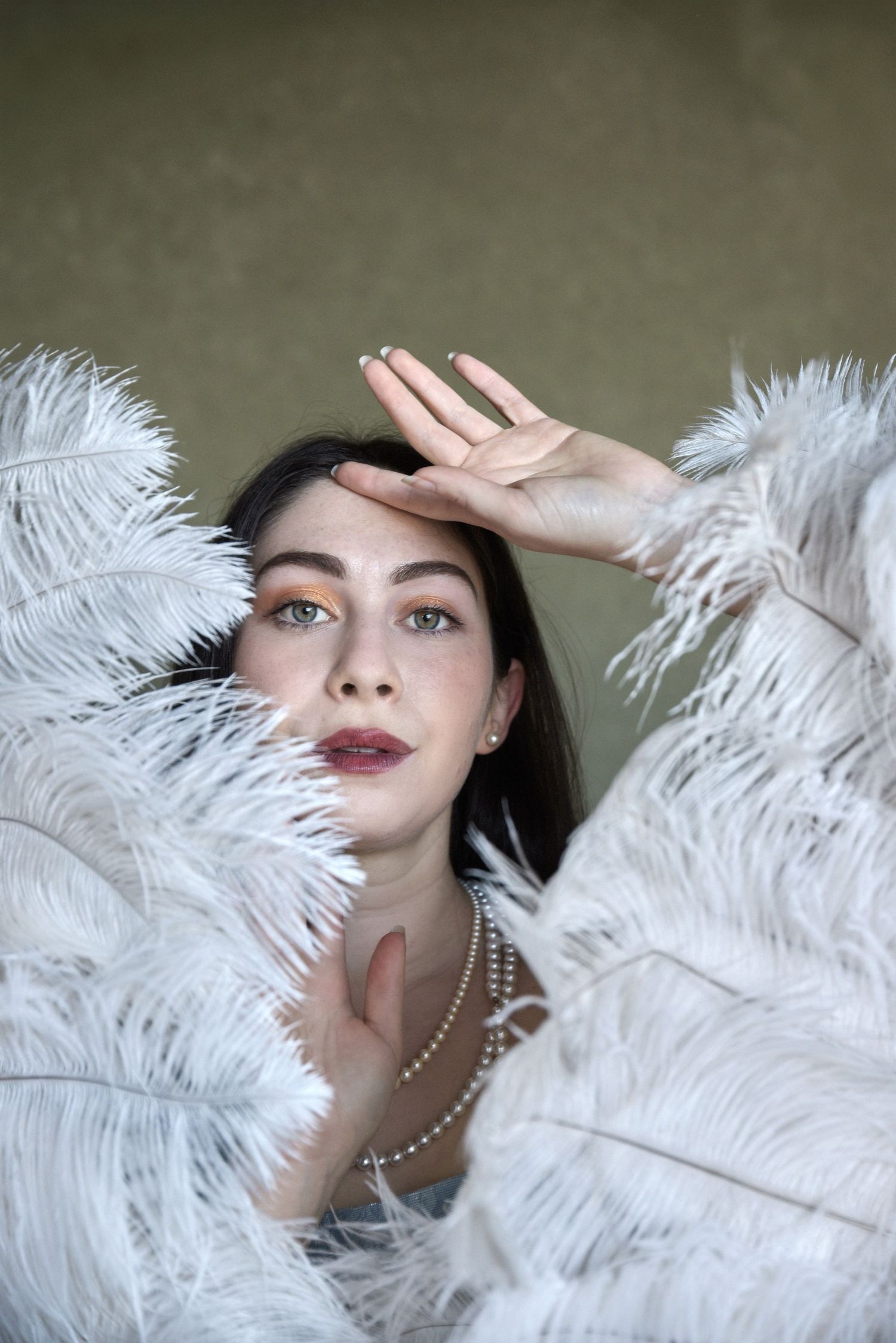 Glamorous portrait with white feathers and pearl necklace in soft lighting.