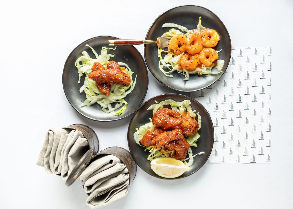 Three dark plates of crispy fried shrimp over shredded cabbage with spicy sauce, served with lemon wedges.