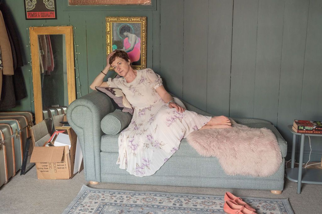 Woman in floral dress reclines on sage green chaise lounge in eclectic decorated room.