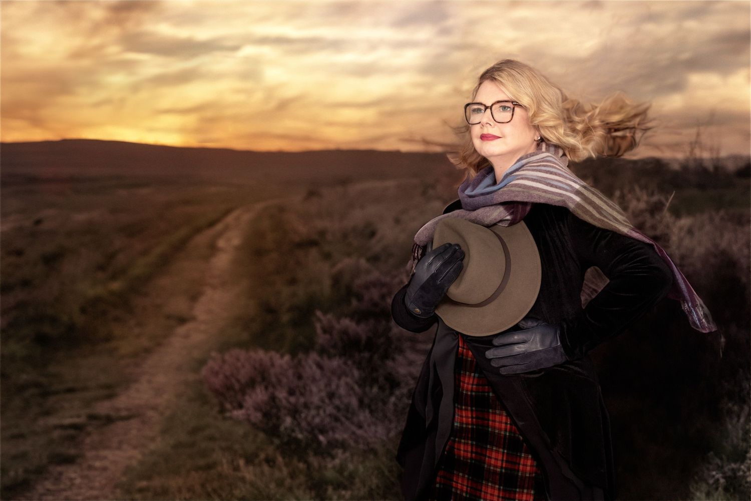 Atmospheric sunset landscape photo with person in plaid skirt and flowing scarf on rural path.