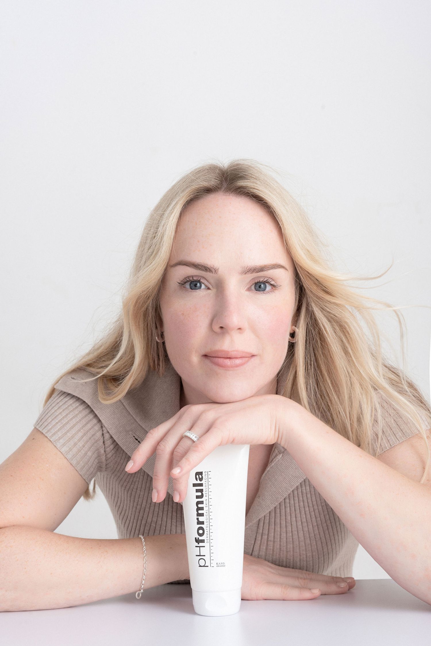 Professional beauty product advertisement showing a model resting on a white table with a skincare product.