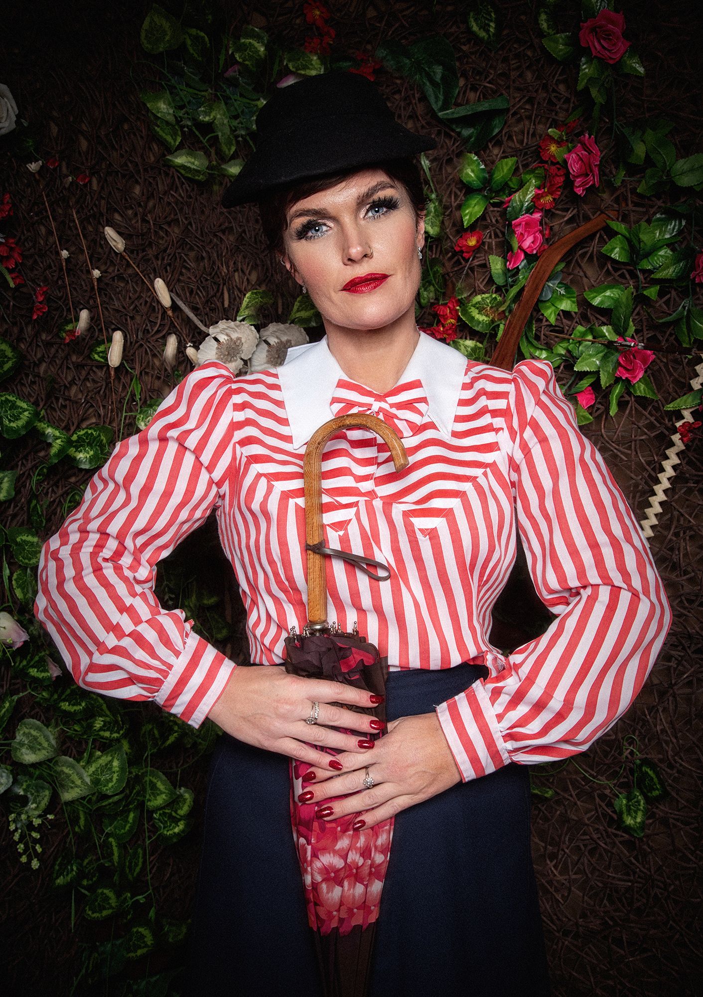 A stylized portrait with red and white striped blouse, black hat, and floral backdrop.