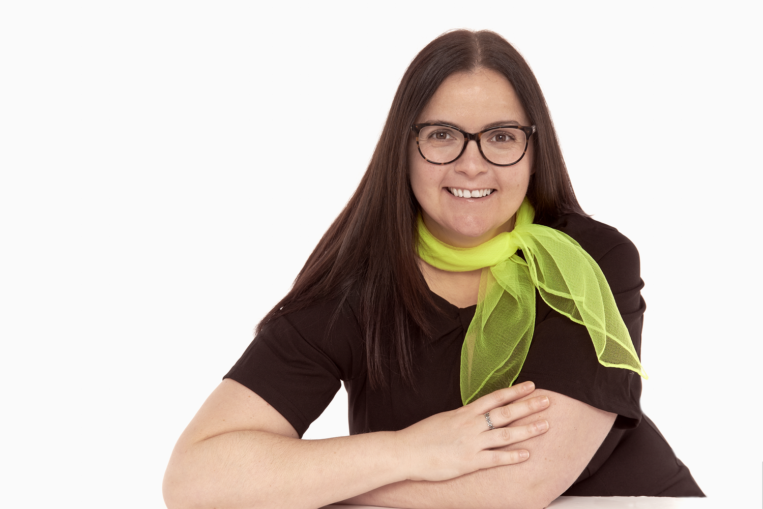 Portrait in black top with lime green scarf and glasses against white background.