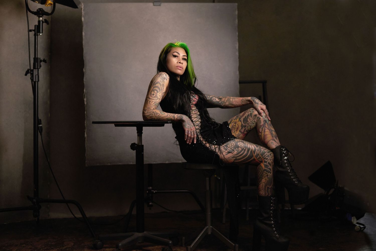 Alternative model with green hair and tattoos posing in studio setting.